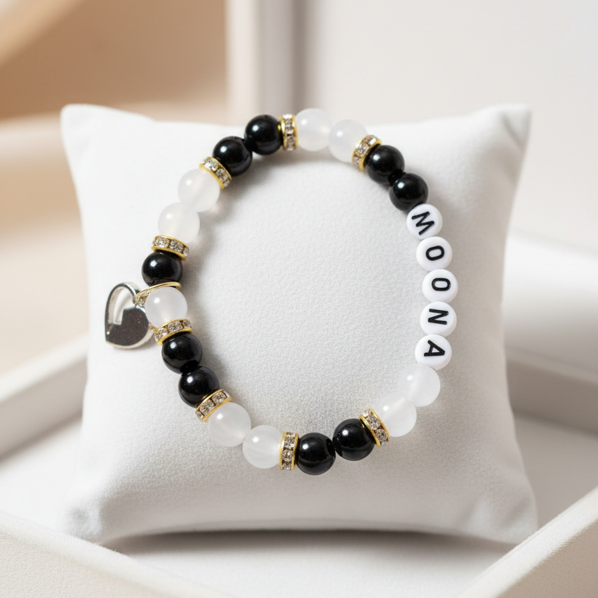 Black, white, and gold beaded bracelet on a white pillow with 'MOONA' branding.