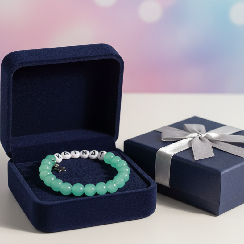Green beaded bracelet in an open navy blue jewelry box with a wrapped gift next to it on a white surface.
