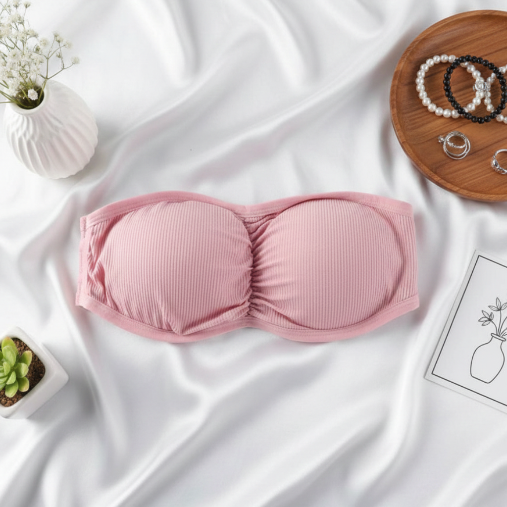 Pink bralette on a white fabric background with jewelry and plants.