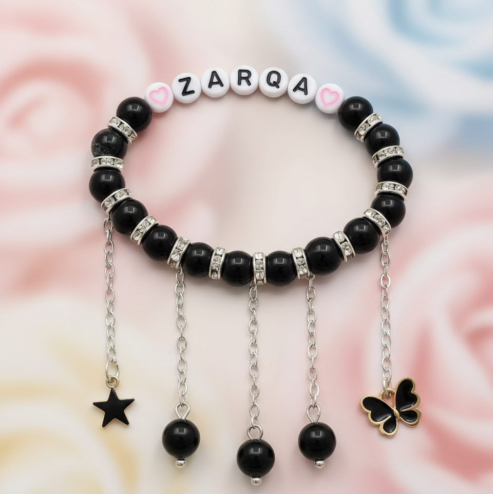 Black beaded bracelet with charms on a soft pink background