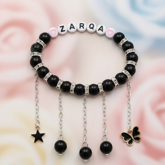 Black beaded bracelet with charms on a soft pink background