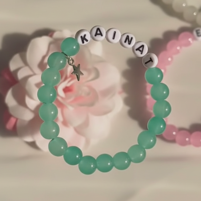 Green beaded bracelet with 'KAINAT' charm on a floral background