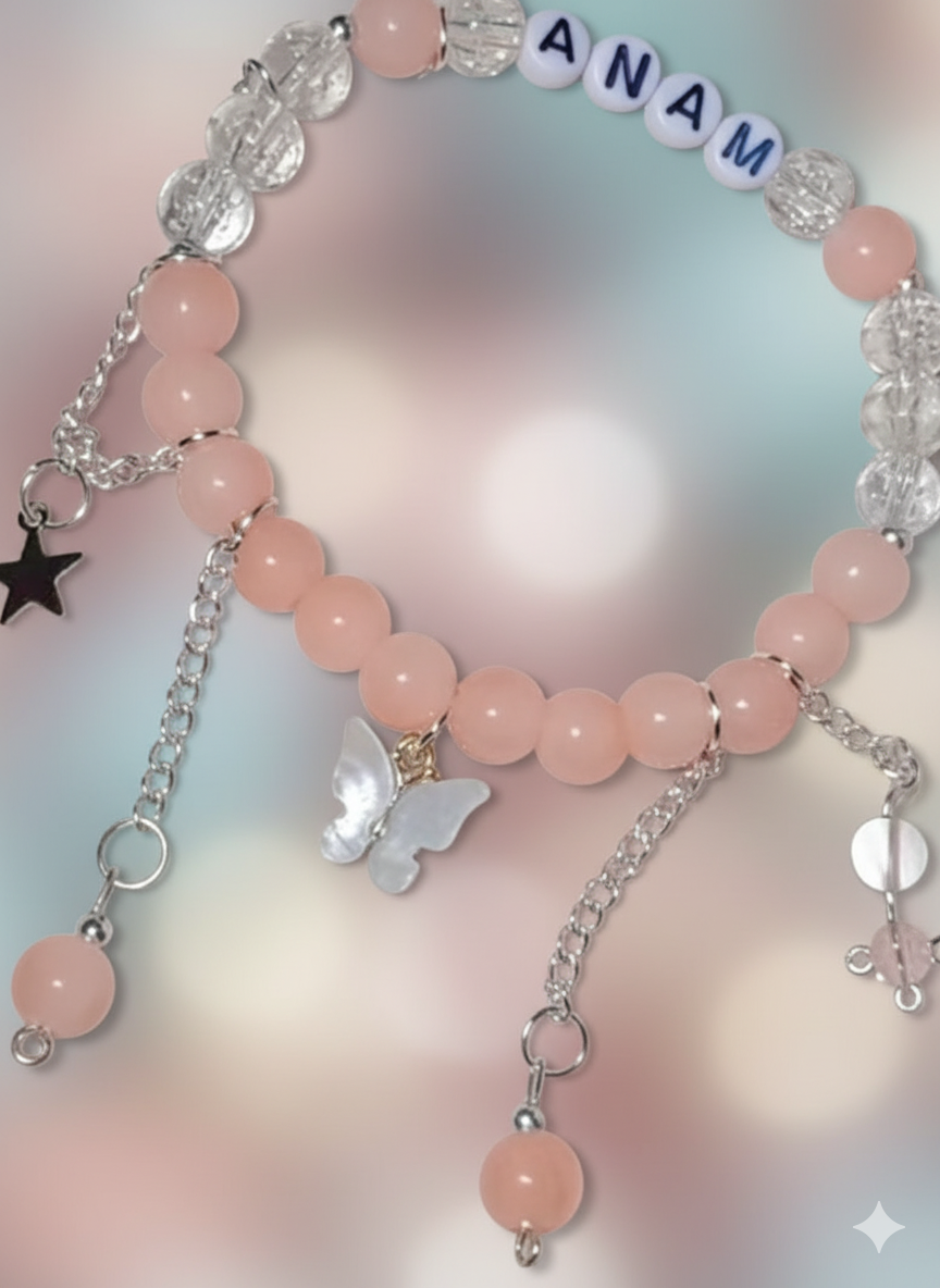 Pink beaded bracelet with charms and 'ANAM' beads on a soft pink background