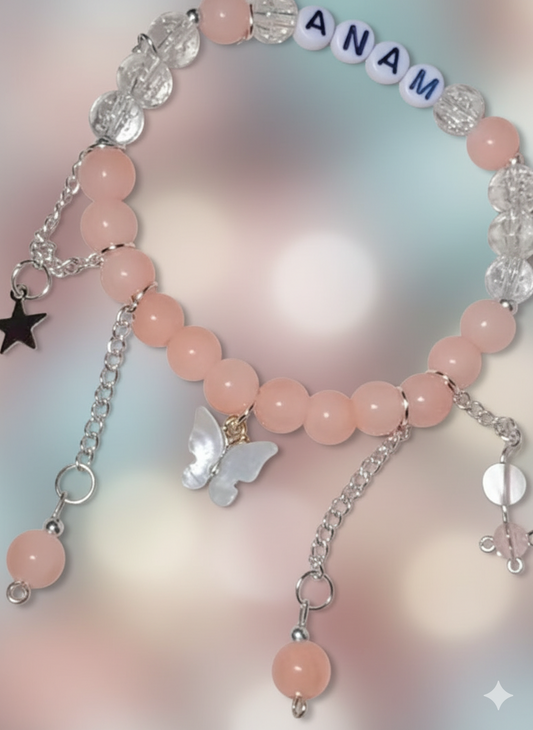 Pink beaded bracelet with charms and 'ANAM' beads on a soft pink background